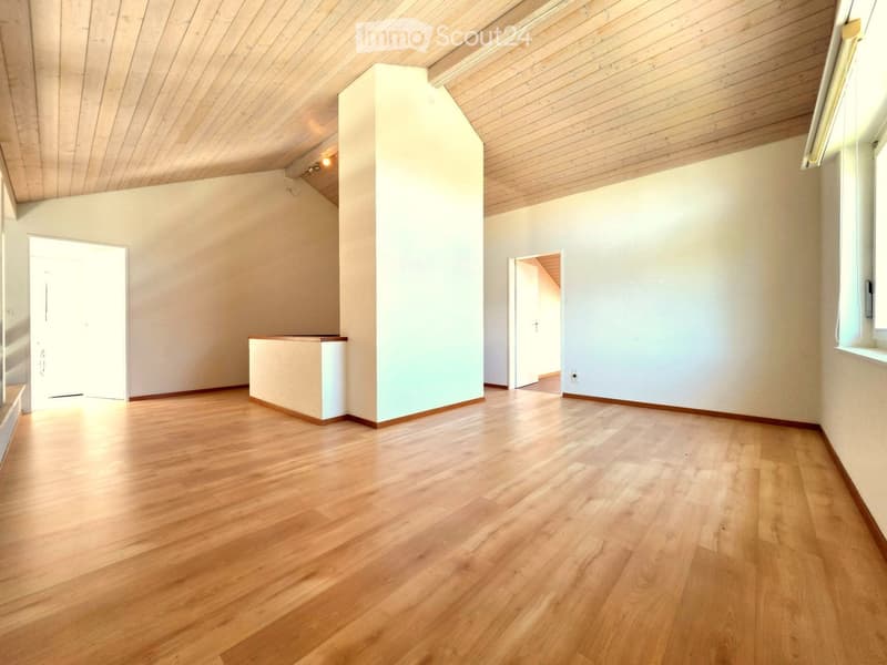Empty room with wooden flooring, white walls, and a slanted wooden ceiling. Two doorways lead to adjacent spaces.