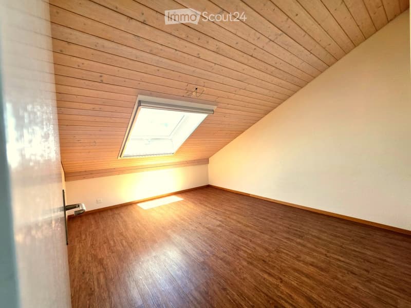 Empty room with wooden floor, wooden slatted ceiling, and a skylight window letting in natural light.