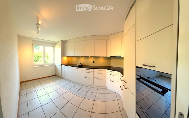 Modern kitchen with white cabinets, black countertops, and a tiled floor. Features a window with a view of greenery, under-cabinet lighting, and a built-in sink with a faucet.