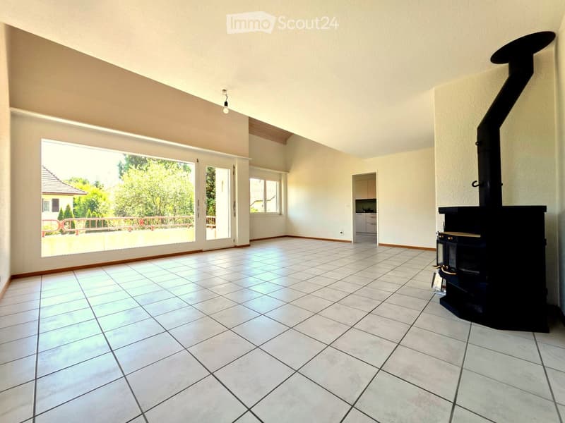 Empty room with tiled floor, fireplace, large window with sliding doors leading to a balcony, and a small adjacent kitchen area.