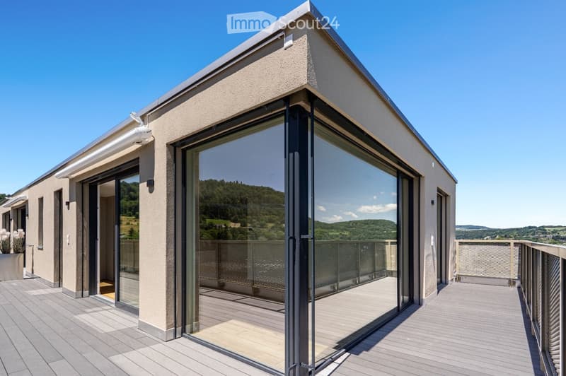 Modern balcony with large glass doors, wooden decking, and scenic mountain view.