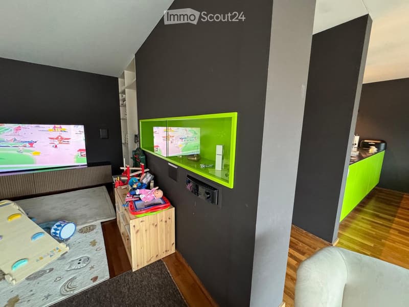 Modern living room with a large screen, a sofa, a wooden table, and a green cabinet with shelves.