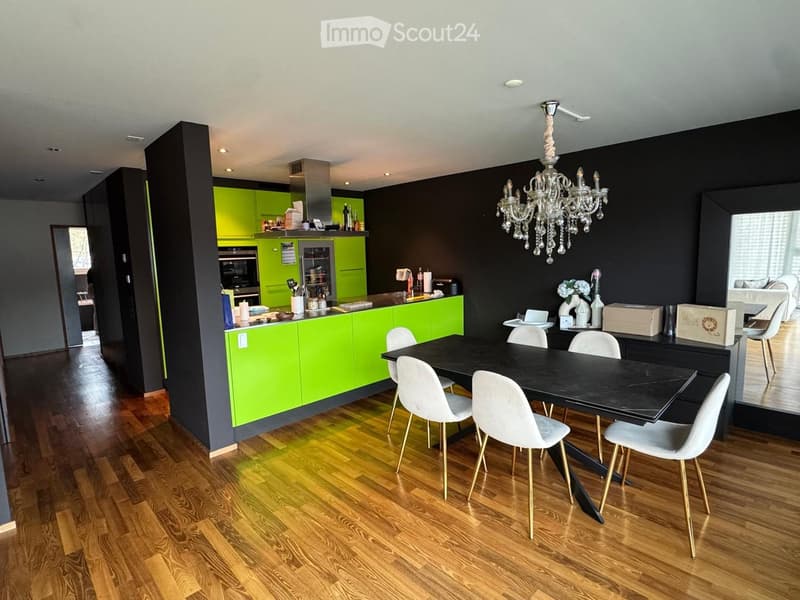 Modern kitchen and dining area with green cabinets, a black dining table with six white chairs, a chandelier, and various kitchen appliances.