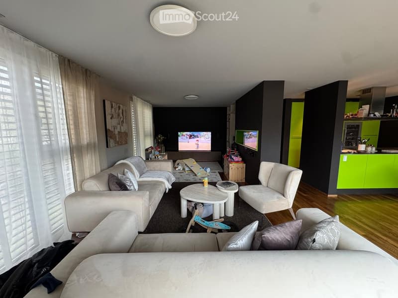Modern living room with a white sectional sofa, coffee table, armchair, and a small kitchen area with green cabinets.