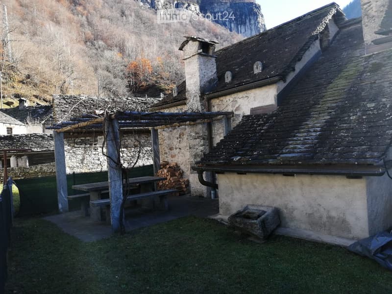 Outdoor area with a stone building, wooden bench, and a stack of firewood.