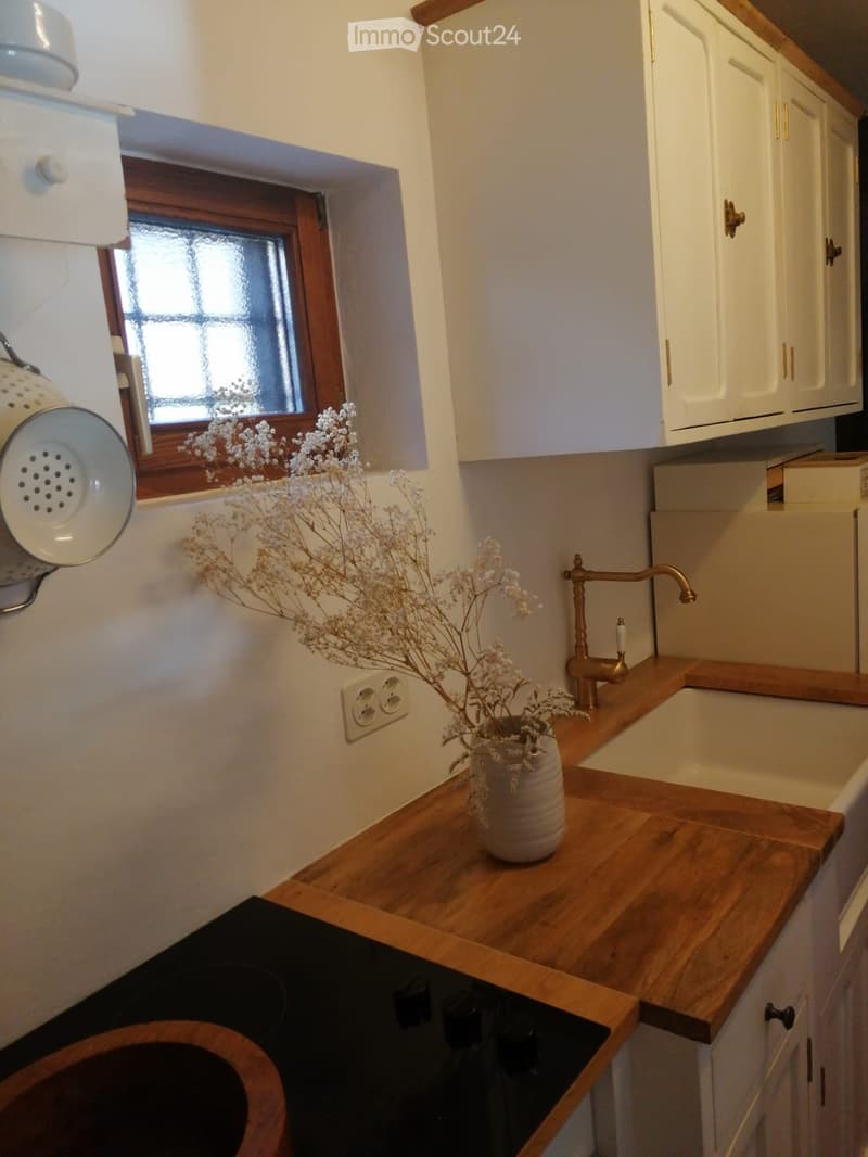 A cozy kitchen with wooden countertops, white cabinets, a sink with a brass faucet, and a decorative vase with dried flowers on the counter.