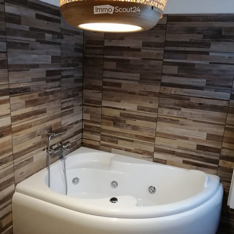Modern bathroom with a white bathtub, wooden wall tiles, and a sleek hanging light fixture.