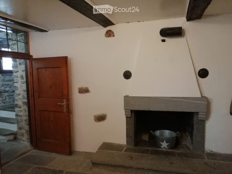 Empty room with a stone fireplace, wooden door, and exposed wooden beams on the ceiling.