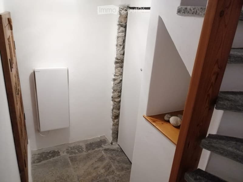 Narrow hallway with stone walls, wooden staircase, and a white panel on the left side.
