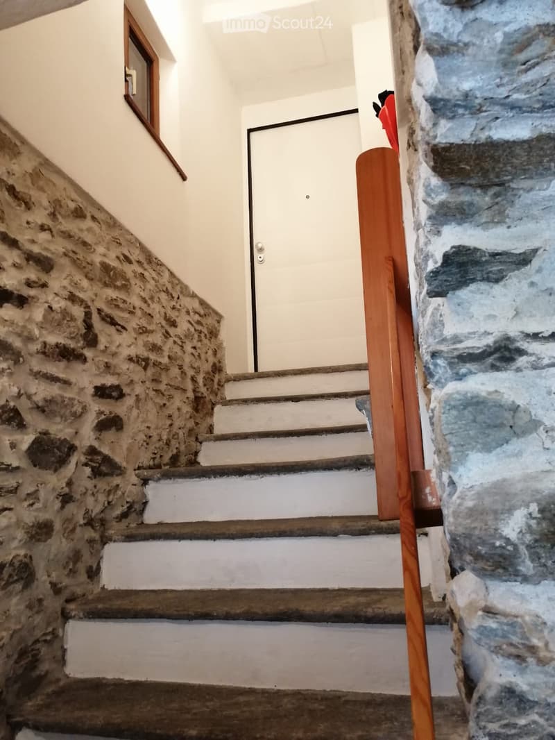 Staircase with stone walls, wooden handrail, and a white door at the top.