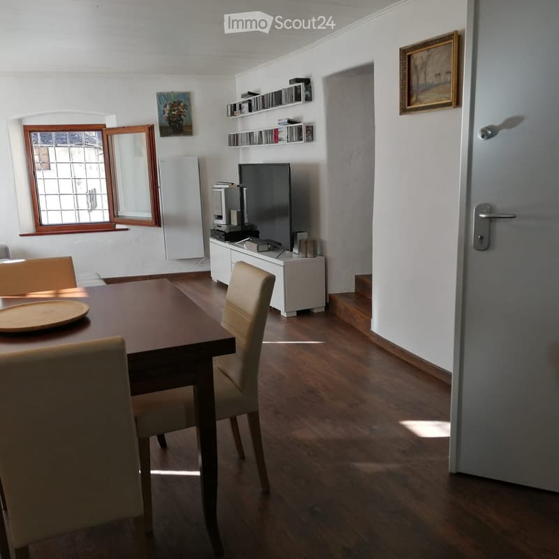 Dining area with wooden table, chairs, TV, refrigerator, shelves, and artwork on the walls.