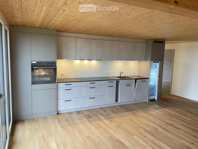 Modern kitchen with grey cabinetry, wooden flooring, built-in oven, sink, and refrigerator.