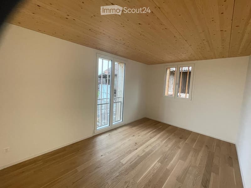 Empty room with wooden flooring, white walls, and large windows, including a sliding glass door leading outside.