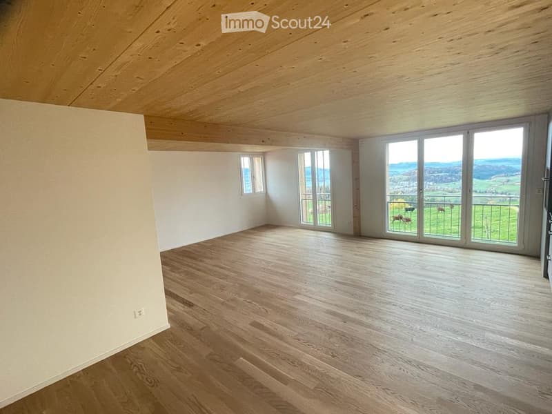 Empty room with wooden floor, white walls, large windows, and a view of a green landscape.