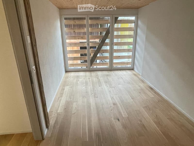 Empty room with light wooden flooring, white walls, and a large sliding glass door leading outside.