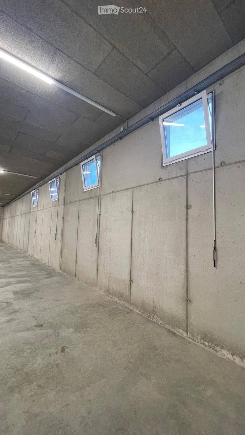 Empty concrete corridor with small windows along one wall and a raised ceiling with fluorescent lighting.