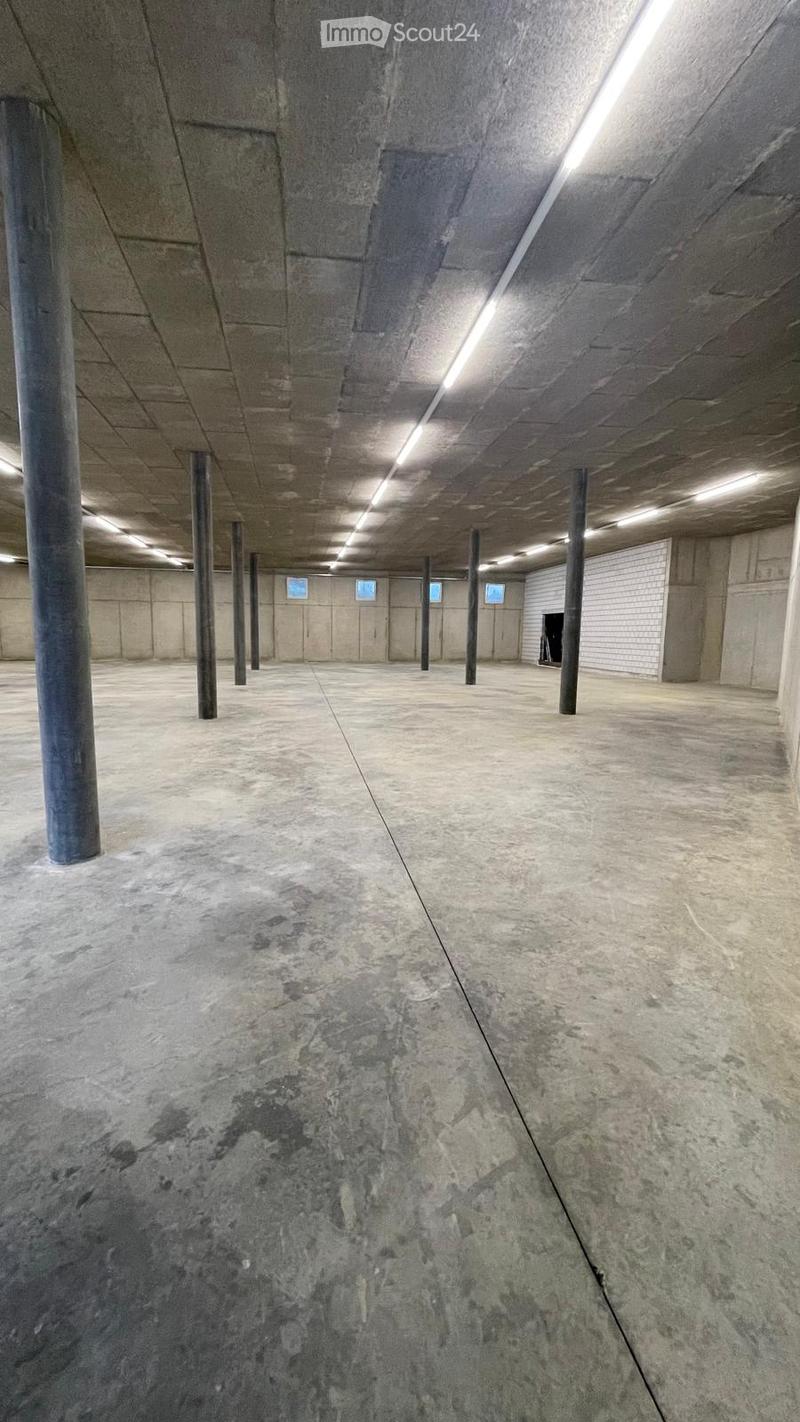 Empty underground parking area with concrete floors and pillars, fluorescent lighting, and closed garage doors.