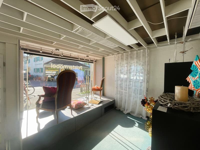 A room with a glass window, chairs, pillows, and a candle on a table