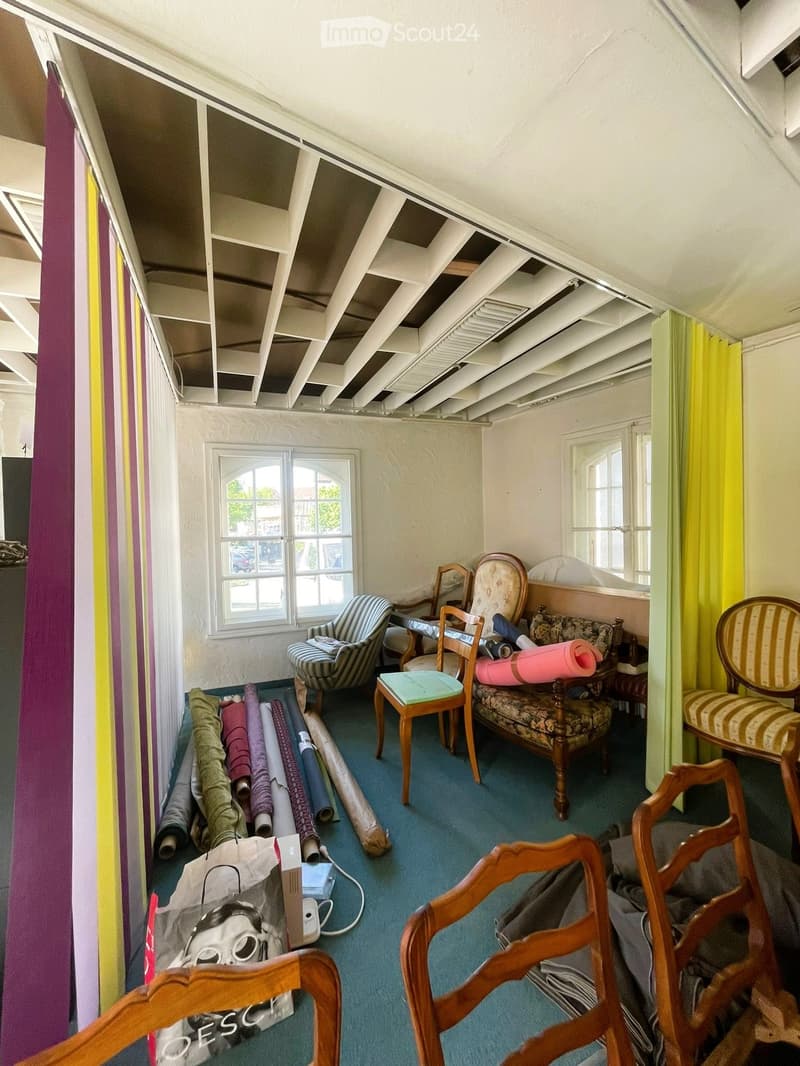 room with white walls, wooden chairs, windows, carpet, and various items on the floor