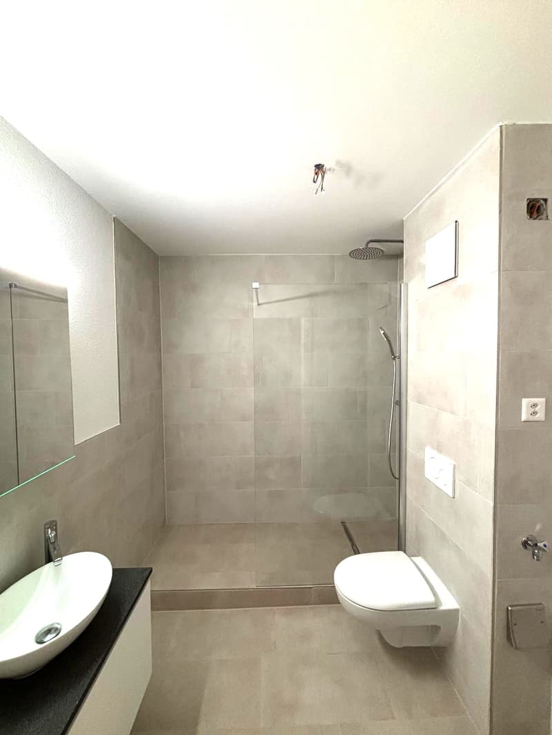 Modern bathroom with a white sink, toilet, and glass-enclosed shower. Light-colored tiles and sleek fixtures.