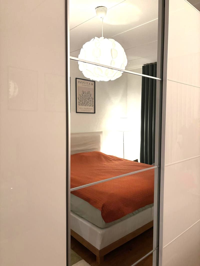 Modern bedroom with a single bed, orange blanket, a hanging spherical lamp, and a picture frame on the wall.