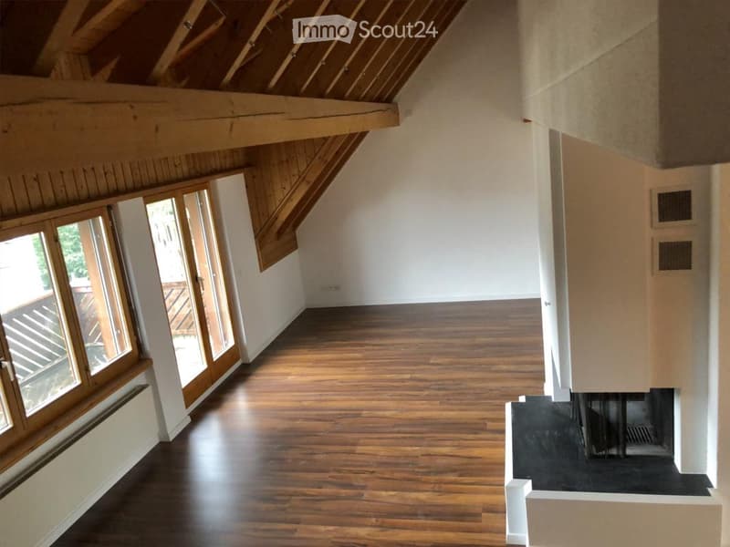 Empty room with wooden flooring, white walls, large windows, and exposed wooden beams on the ceiling.