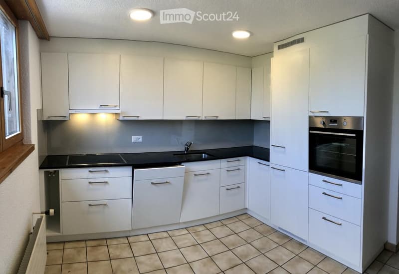 Modern kitchen with white cabinets, black countertops, and built-in oven. Features include a sink with a faucet and recessed lighting.