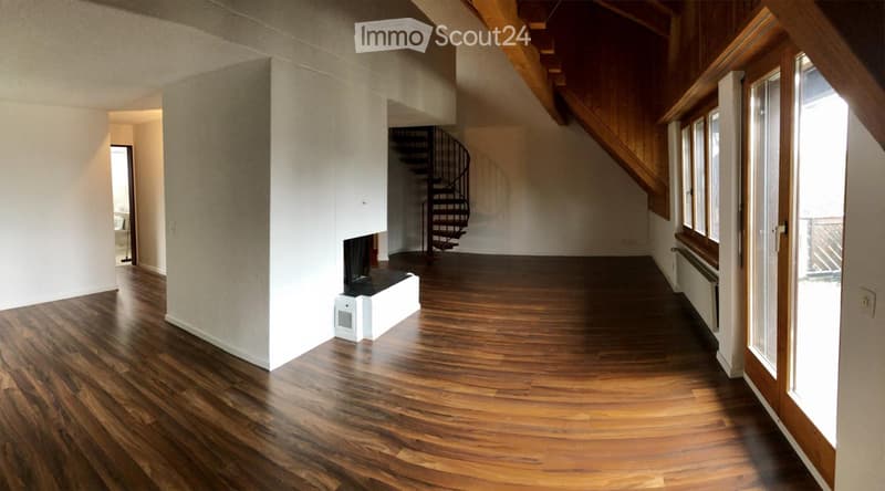 Spacious hallway with wooden flooring, curved design, fireplace, spiral staircase, large windows, and open doorway leading to another room.