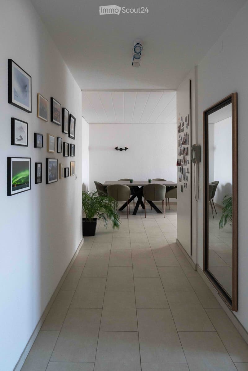 Dining area with a modern dining table, chairs, and a potted plant, surrounded by framed artwork on the walls.