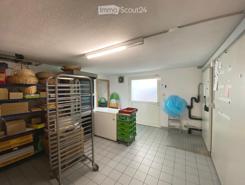 Empty room with white walls, carpeted floor, and a window. Shelves with storage items are visible along one wall.