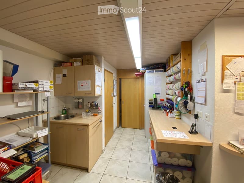 A narrow hallway with wooden flooring, white tiled ceiling, and storage shelves on both sides filled with various items and supplies.