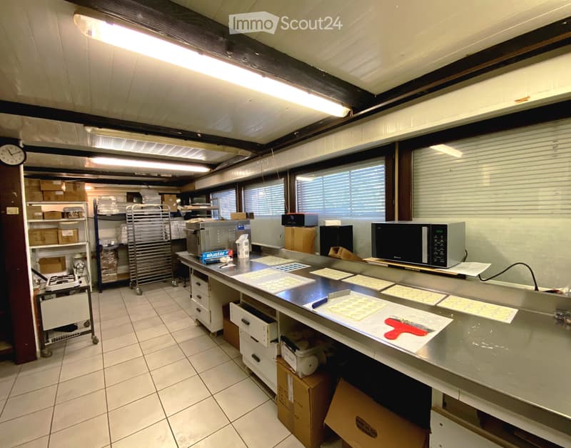 Commercial kitchen with stainless steel appliances, microwave, refrigerator, oven, and storage boxes on shelves.