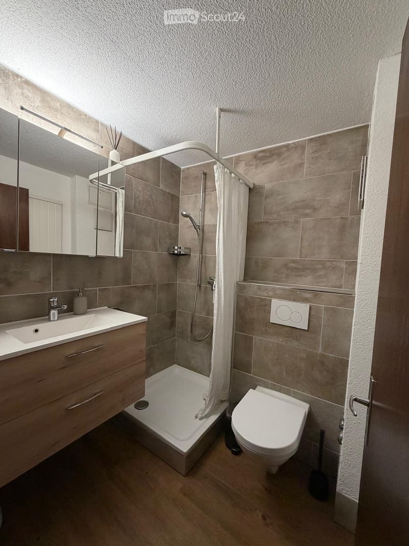 Modern bathroom with a sink, toilet, bathtub, and shower area. Features a wooden cabinet, mirror, and tiled walls.
