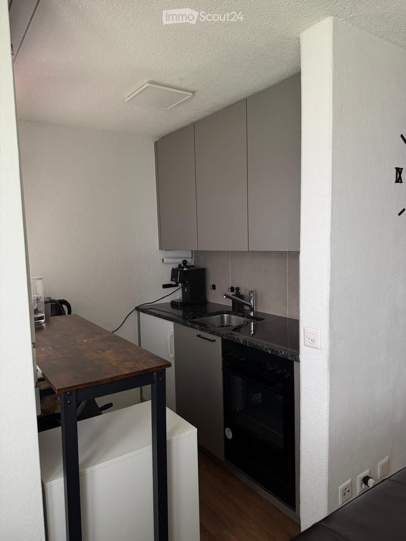 Modern kitchen with grey cabinets, a wooden table, coffee maker, sink, and oven.