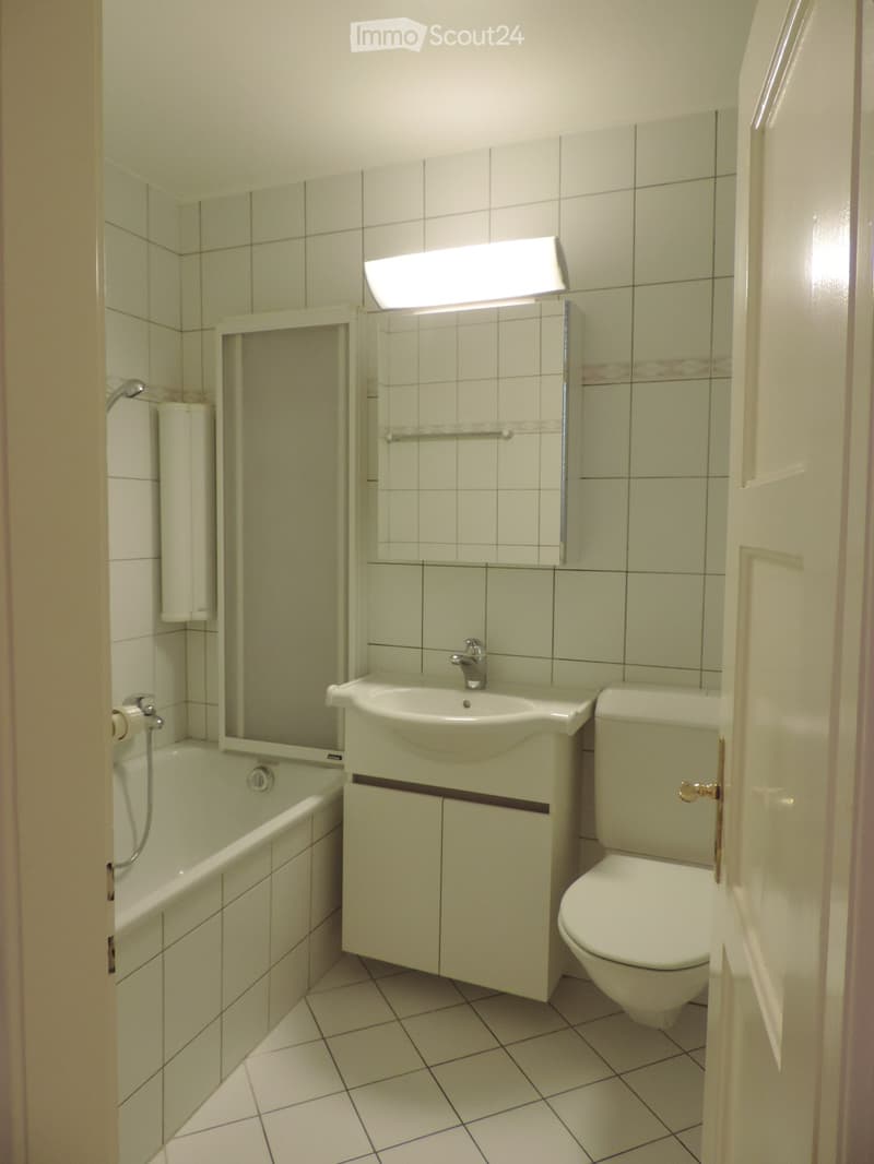 Bathroom with tiled walls and floor, featuring a bathtub, sink, toilet, and mirror with a light fixture above it.