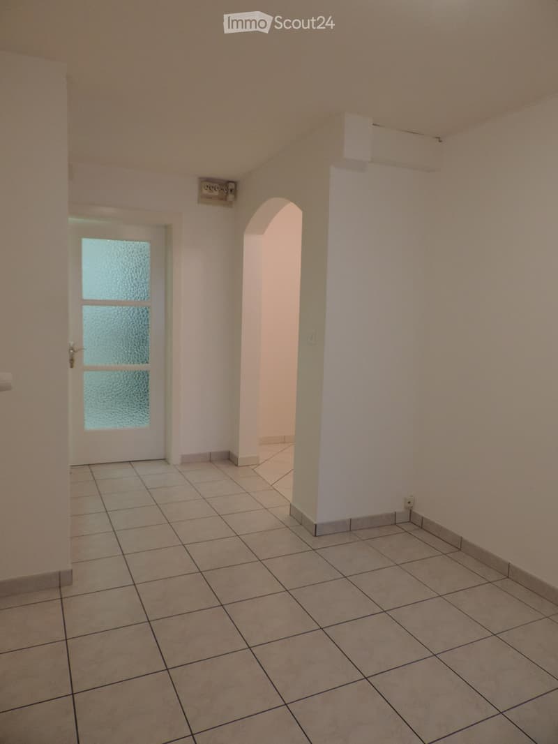 Empty hallway with tiled floor, white walls, and a frosted glass door leading to another room.