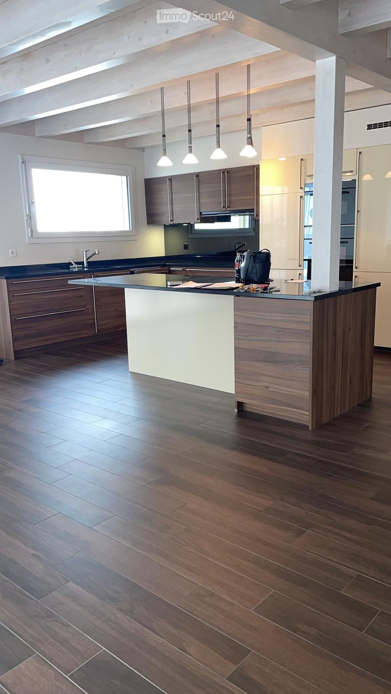 Modern kitchen with wooden flooring, island, pendant lights, and cabinets.