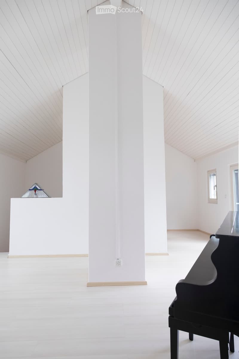 Bright, minimalist room with white walls, a central column, and a grand piano on the right side.