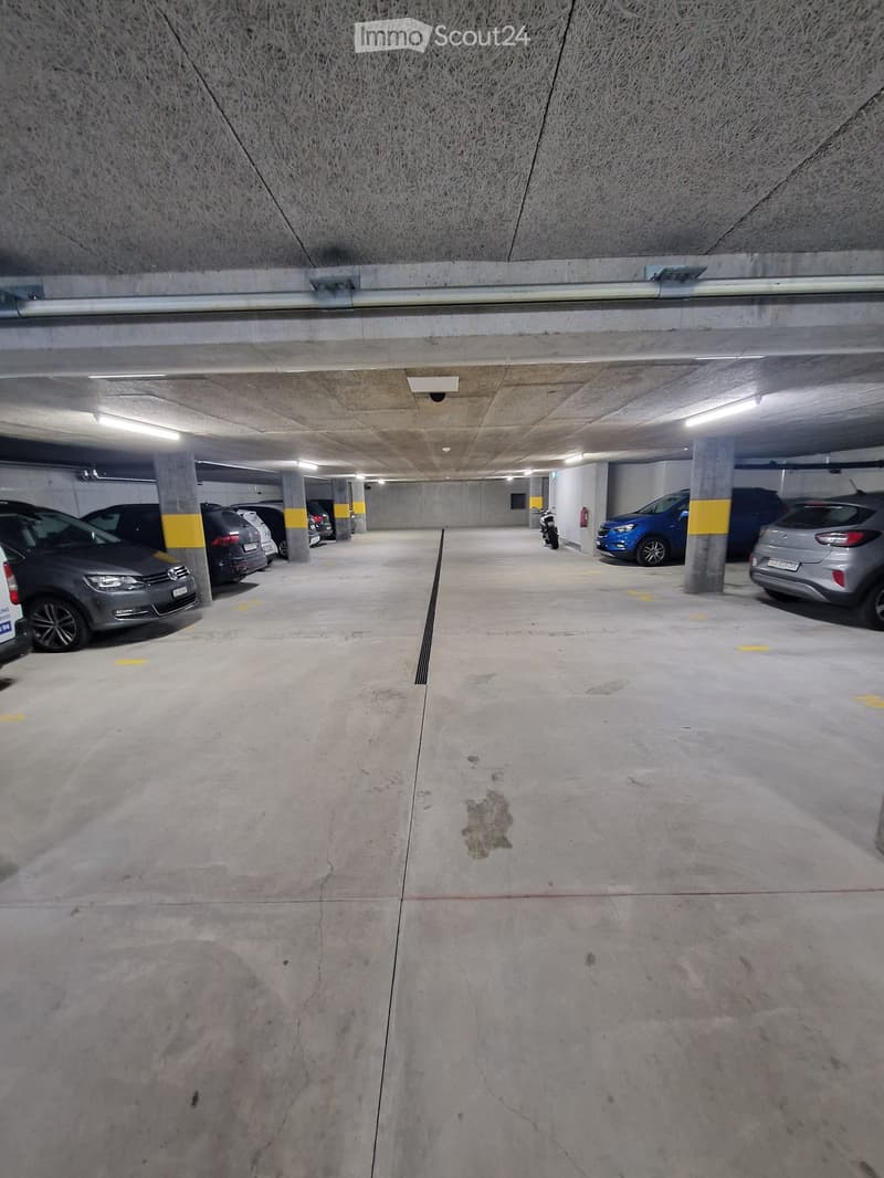 Underground parking area with several parked cars, concrete pillars, and lighting fixtures.