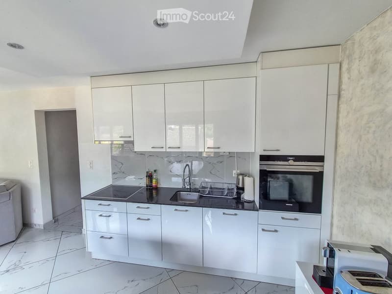 Modern kitchen with white cabinets, marble countertops, and stainless steel appliances including a sink, oven, and toaster.