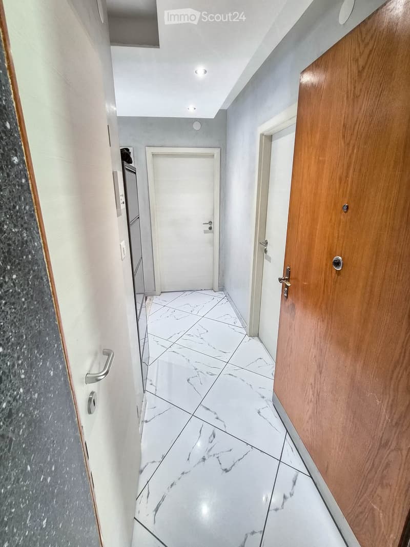 Modern hallway with white marble tiled floor, white walls, and wooden doors on both sides.