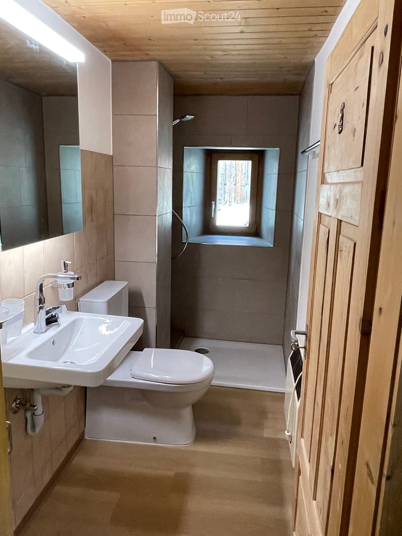Modern bathroom with a sink, toilet, bathtub, and mirror. The space features wooden cabinetry and a window above the bathtub.
