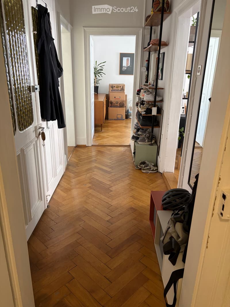 Hallway with herringbone wooden flooring, coat rack, shelves with shoes, and a small table with a helmet and bag.