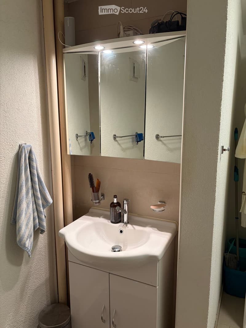 Bathroom with a white sink, mirror with built-in lighting, toothbrush holder, and a towel hanging on the wall.