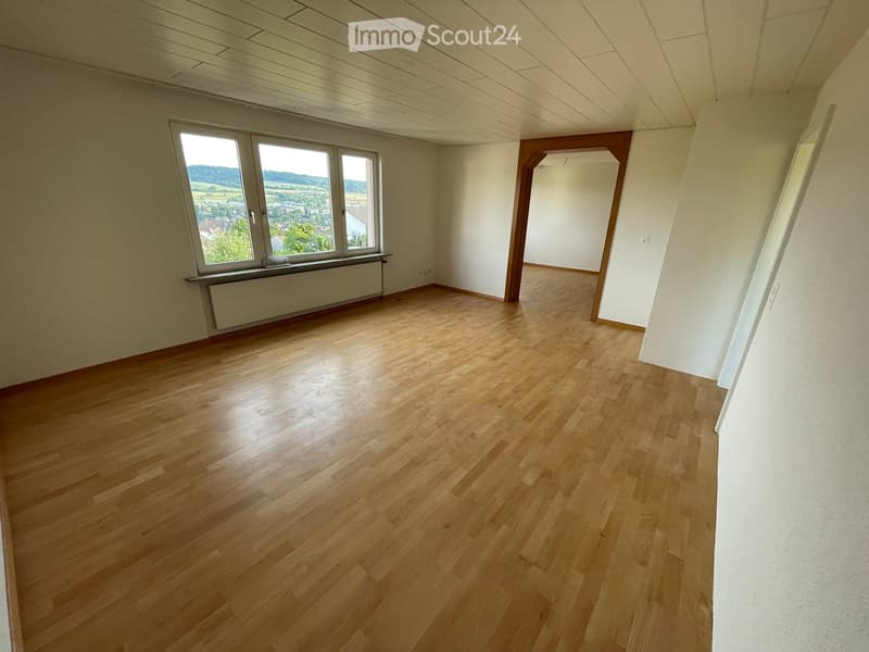 Empty room with wooden flooring, white walls, and large windows offering a view of the landscape.