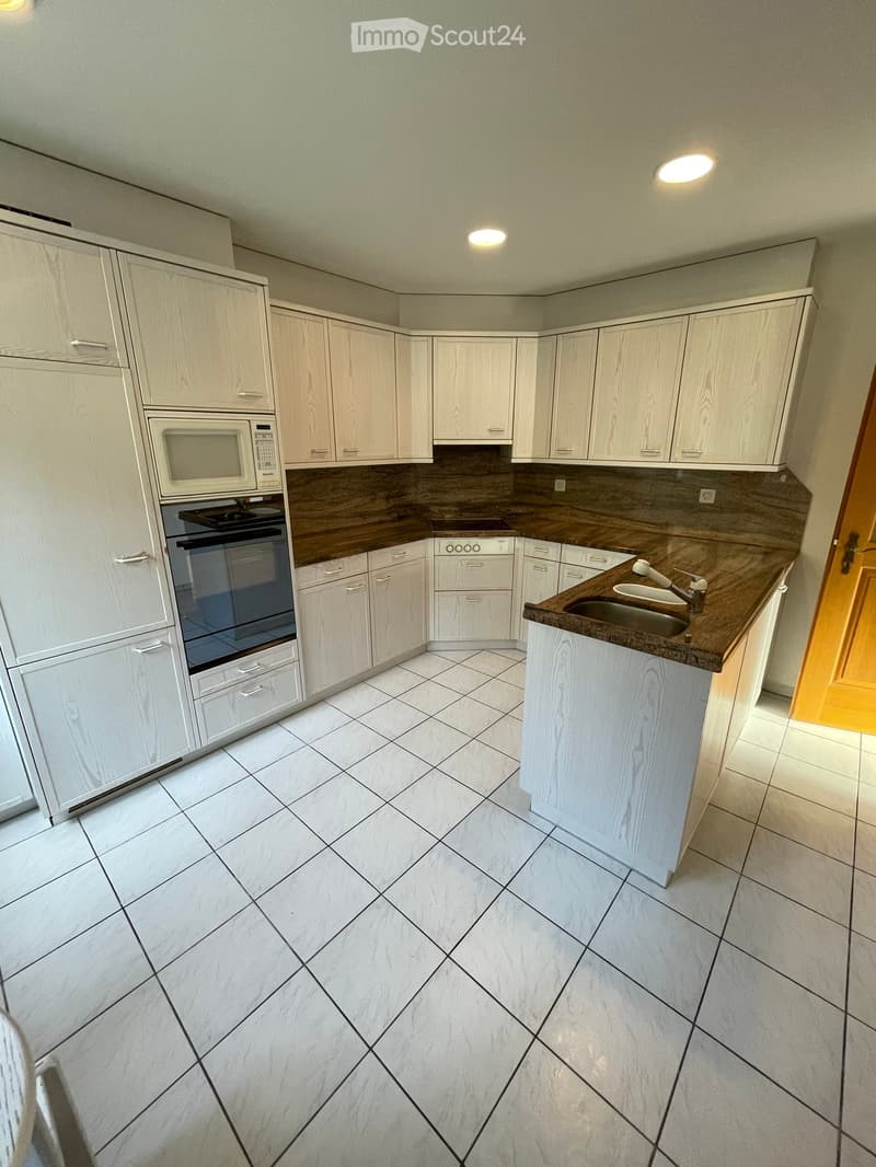 Modern kitchen with white cabinets, wooden countertops, and tiled floor. Features a microwave, oven, and sink.