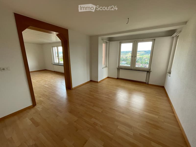 Empty room with wooden flooring, white walls, and large windows offering a scenic view. No furniture or equipment present.