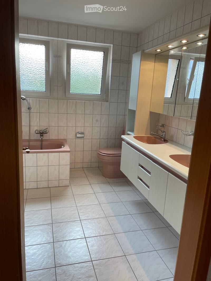 Modern bathroom with tiled walls and floor, featuring a bathtub, toilet, double sink, and mirrored cabinet.