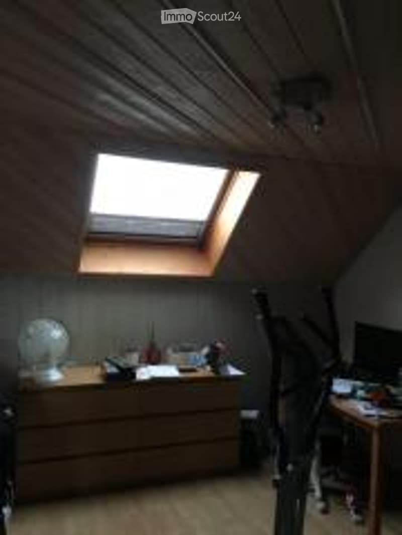 Attic room with wooden walls and floor, skylight window, desk with chair, lamp, and guitar leaning against wall.