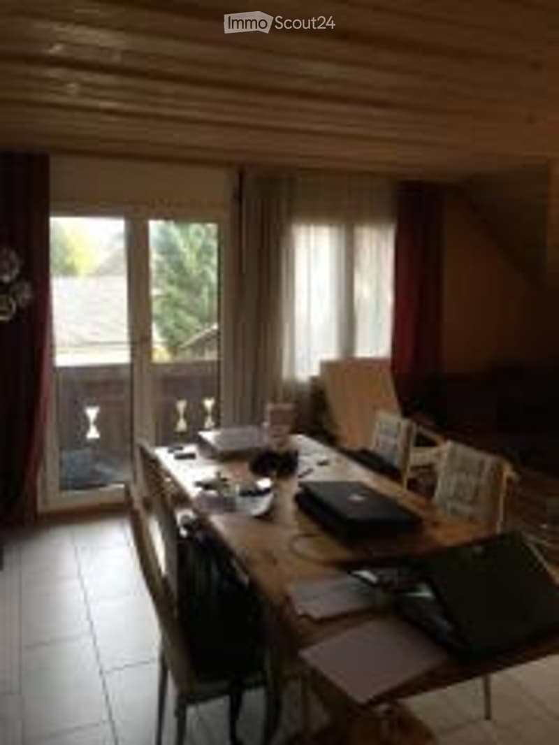 Dining area with wooden table, chairs, laptop, and access to a balcony through large glass doors.